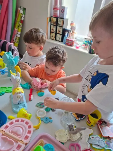Trzech chłopców bawi się Play-Doh i foremkami przy stoliku