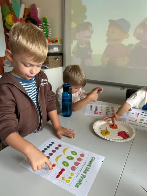 Chłopiec maluje palcem kartę Count the Fruits